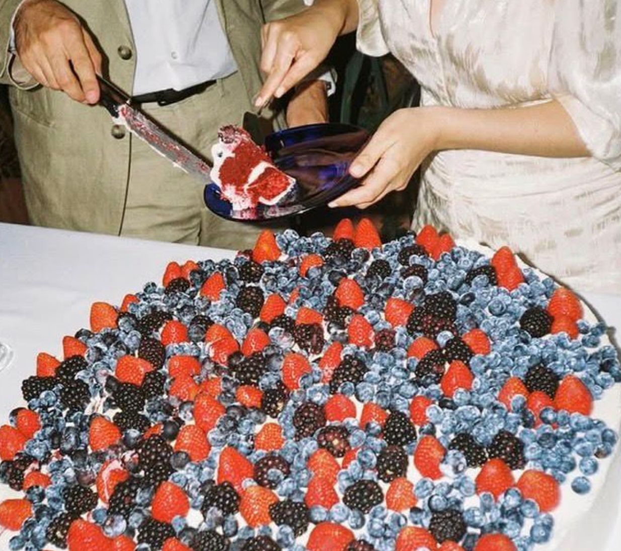 Una pareja cortando una gran tarta con frutos rojos